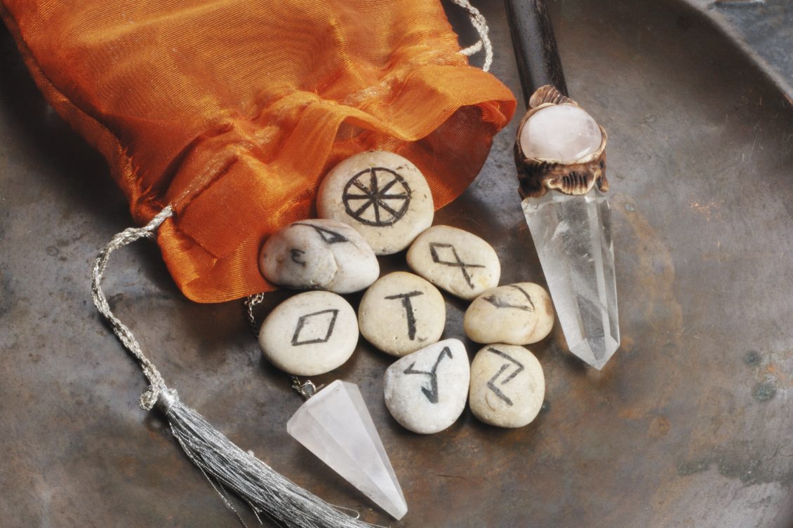 Collection of rune stones, a crystal point, and an orange pouch on a rustic surface.